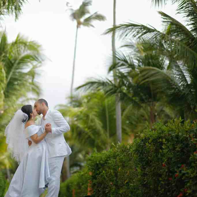 Casal de noivos se beijando enquanto dançam, estão ao ar livre, então tem várias árvores de fundo