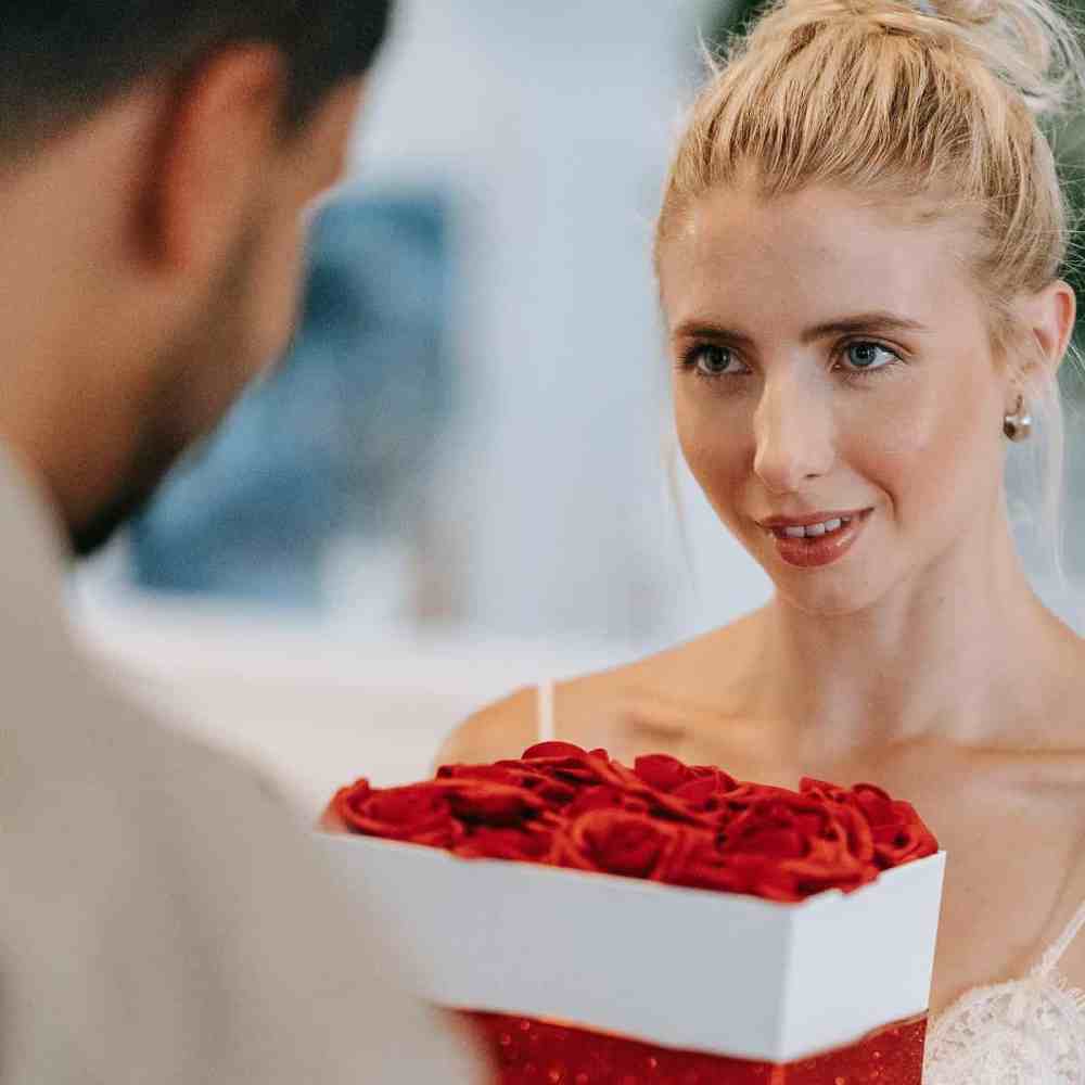 Namorada loiro recebendo caixa de presentes do namorado com pétalas de rosas em cima