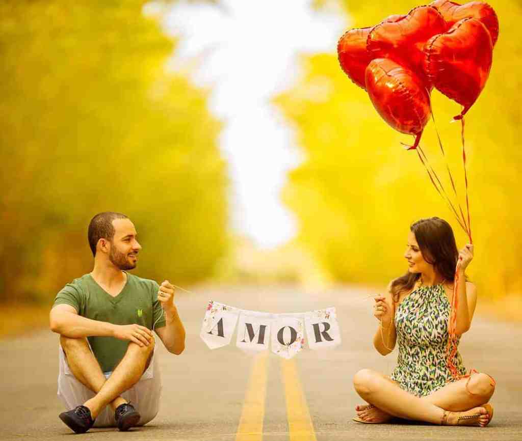 Casal sentado no chão, segurando uma faixa escrita amor e ela segura balões