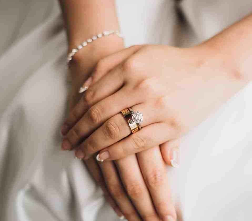 Noiva com as mãos cruzadas na perna, usando joias (aliança e pulseira)