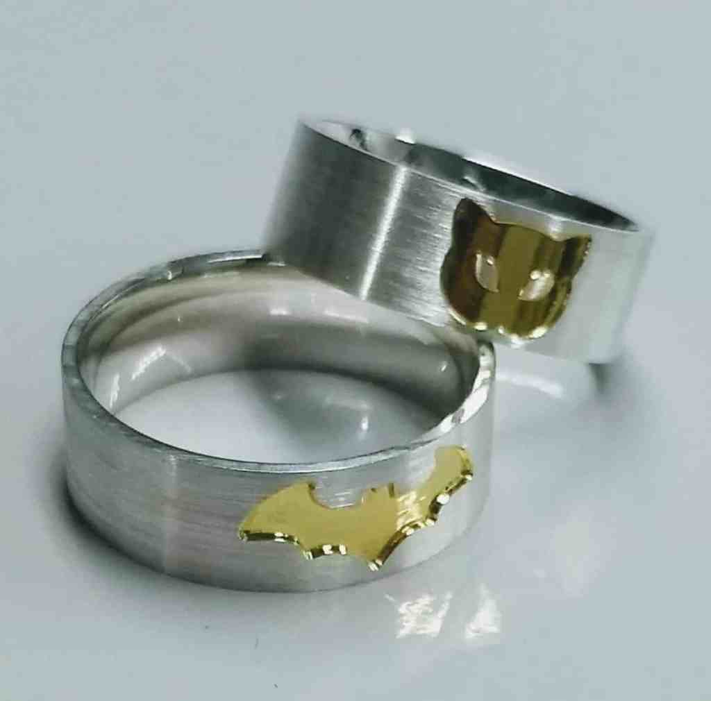 40 frases para pedir em namoro por mensagem - Alianca-de-namoro-batman-e-mulher-gato Duas alianças largas pratas, uma com um símbolo batman (morcego) em ouro amarelo e a outra aliança tem uma gata desenhada em ouro amarelo