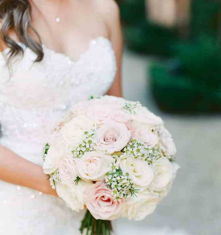 Noiva usando vestido tomara que caia branco segurando buquê redondo de flores brancas