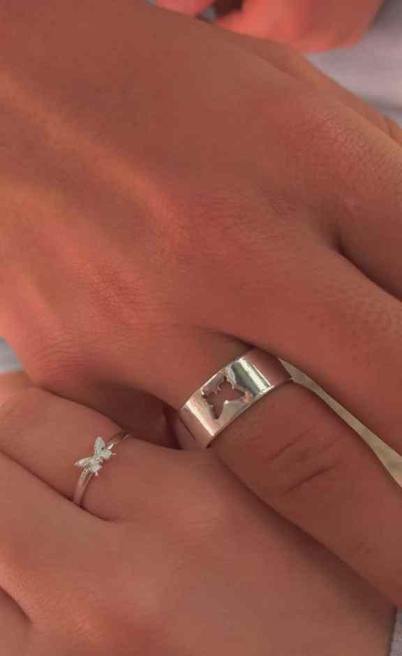 40 frases para pedir em namoro por mensagem - Ideias-de-aliancas-de-namoro Mãos de um casal, ela usa uma aliança fina com uma borboleta no centro, e ele usa uma aliança grossa que tem uma borboleta "faltando" no meio