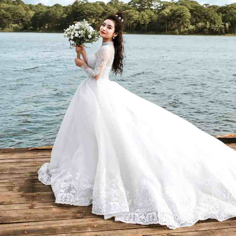 Noiva posando com vestido longo e segurando buquê branco.