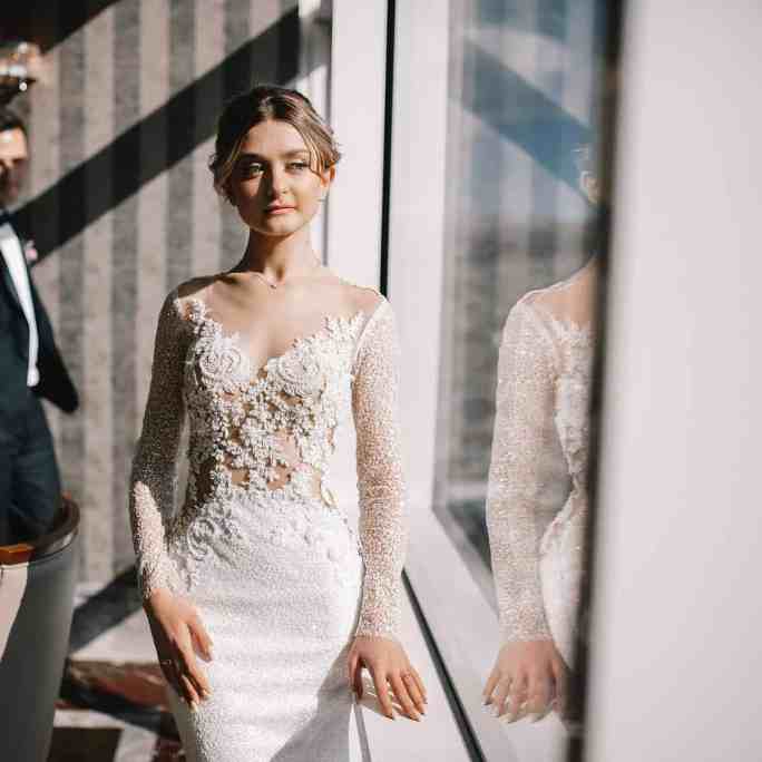 Os 12 Vestidos de Noiva mais Caros do Mundo - Quanto custa vestido de casamento Noiva olhando pela janela e noivo no fundo olhando para ela