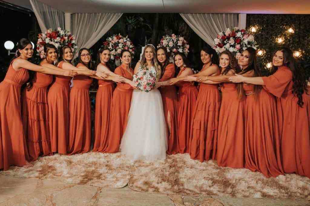 Noiva no centro da imagem com madrinhas em volta com vestido laranja.