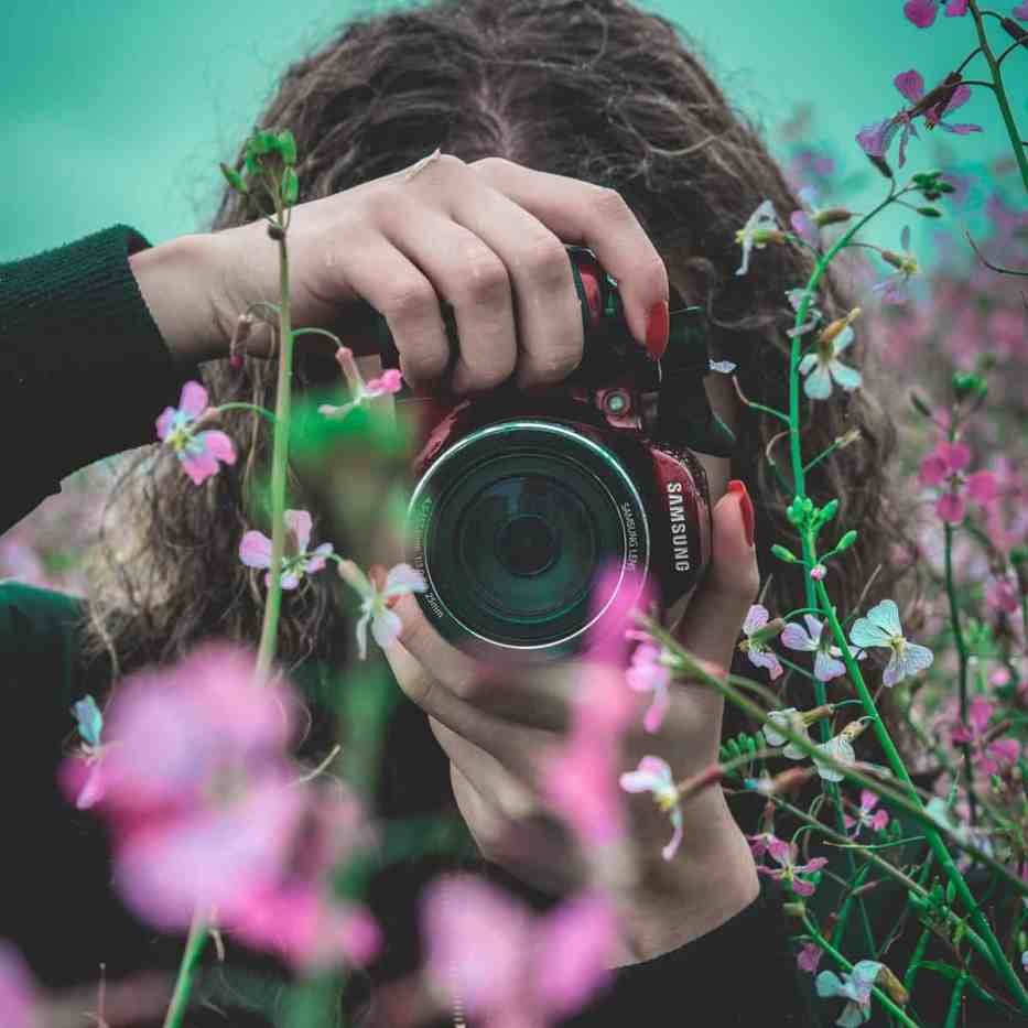 Fotógrafa tirando fotos atrás de algumas flores