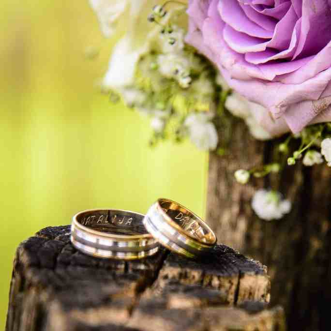 Foto das alianças em cima de um toco de madeira junto com um buquê de flores