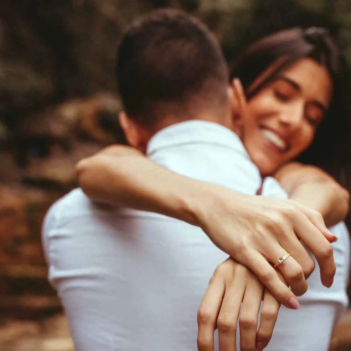 Mulher abraçando o noivo, em seu dedo tem um anel de noivado