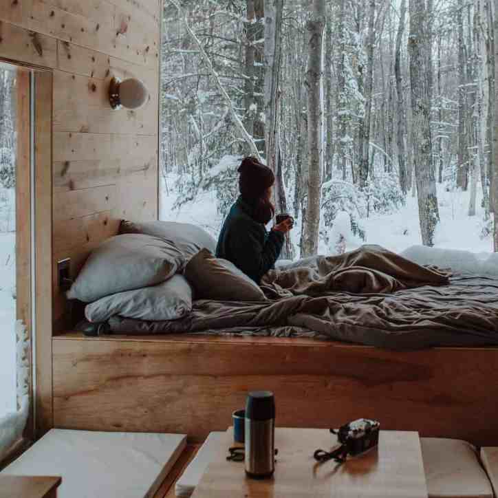 Mulher sentada na cama em uma cabana na floresta que está cheia de neve - 15 coisas que você precisa saber antes de fazer o pedido de casamento