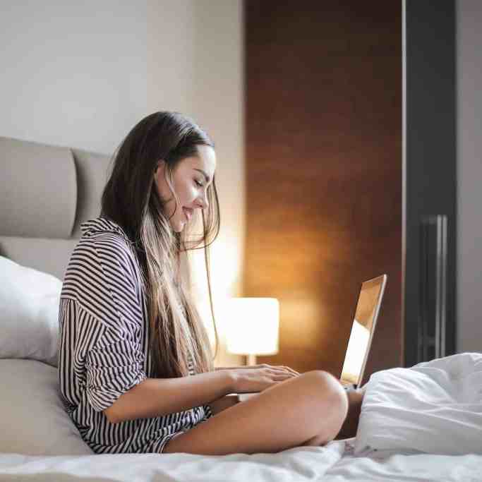 Existe amor nos aplicativos de relacionamento? - Relacionamentoapaplicativo 4 Mulher sentada na cama sorrindo enquanto escreve no computador