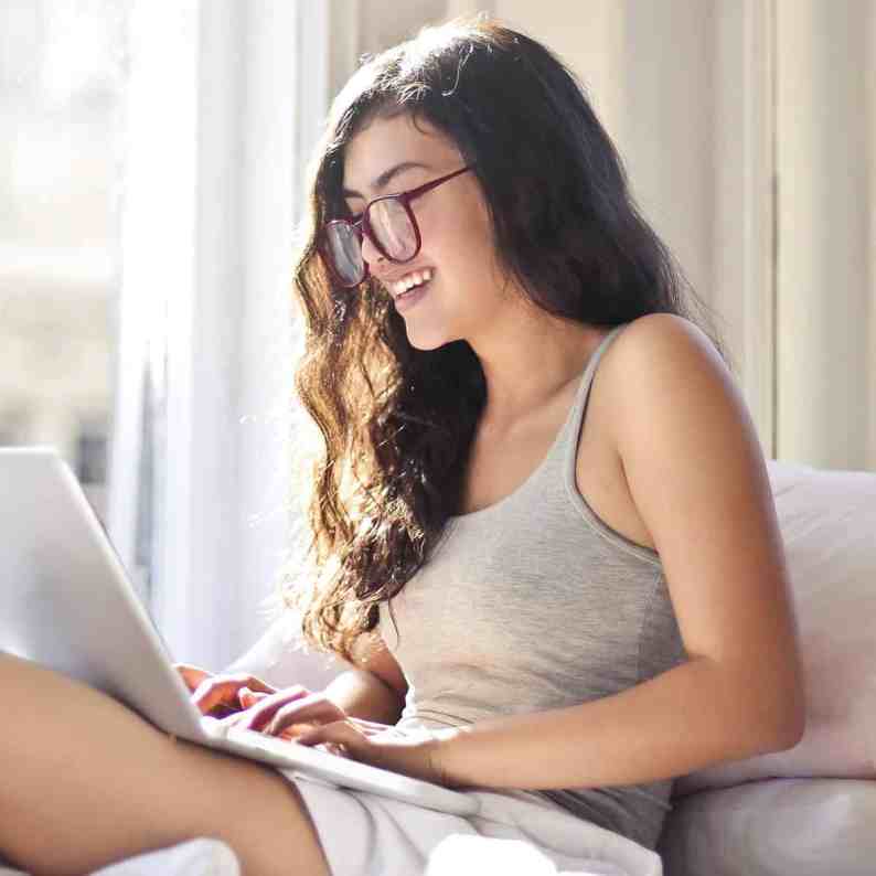 Existe amor nos aplicativos de relacionamento? - Relacionamentoapaplicativo 5 Mulher mexendo no notebook sentada na cama rindo