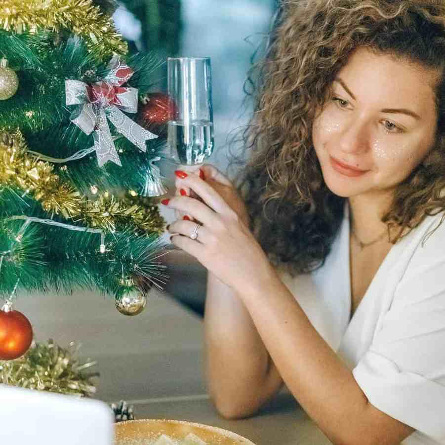 Existe amor nos aplicativos de relacionamento? - Relacionamentoapaplicativo 6 Mulher tomando champagne enquanto tem vídeo chamada, de fundo há decoração de natal