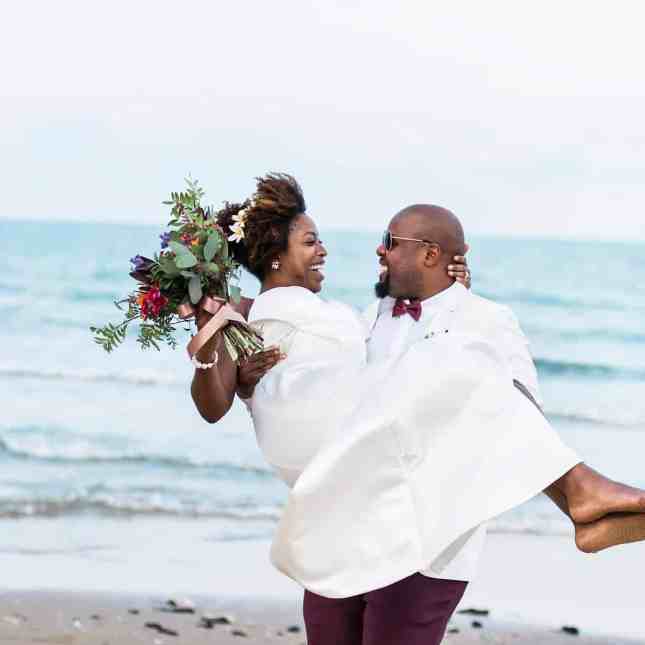 Homem carregando sua noiva no colo pela praia