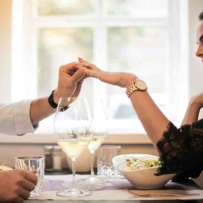 Homem colocando anel de noivado no dedo da namorada durante almoço