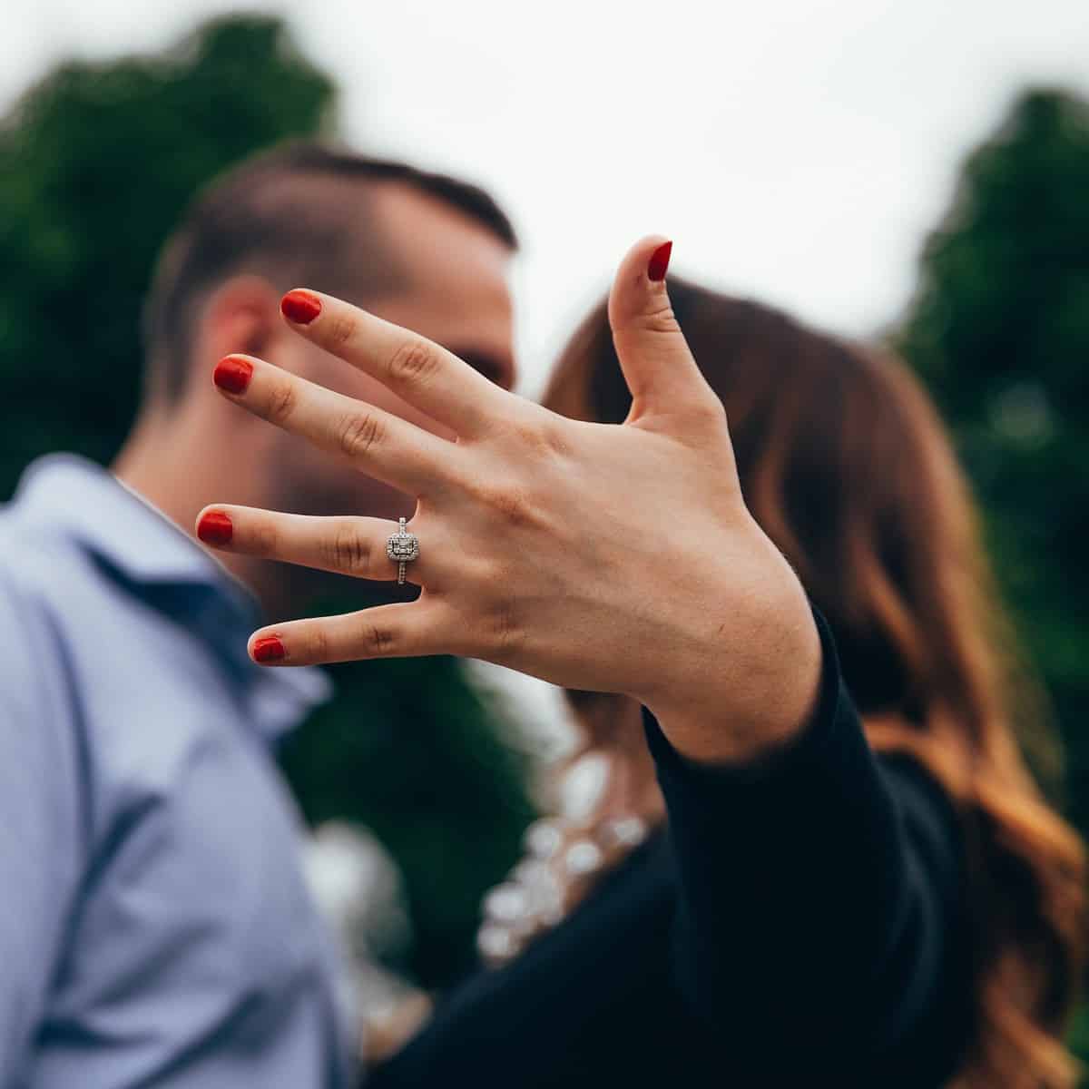 Mulher mostrando seu anel de noivado enquanto beija o noivo