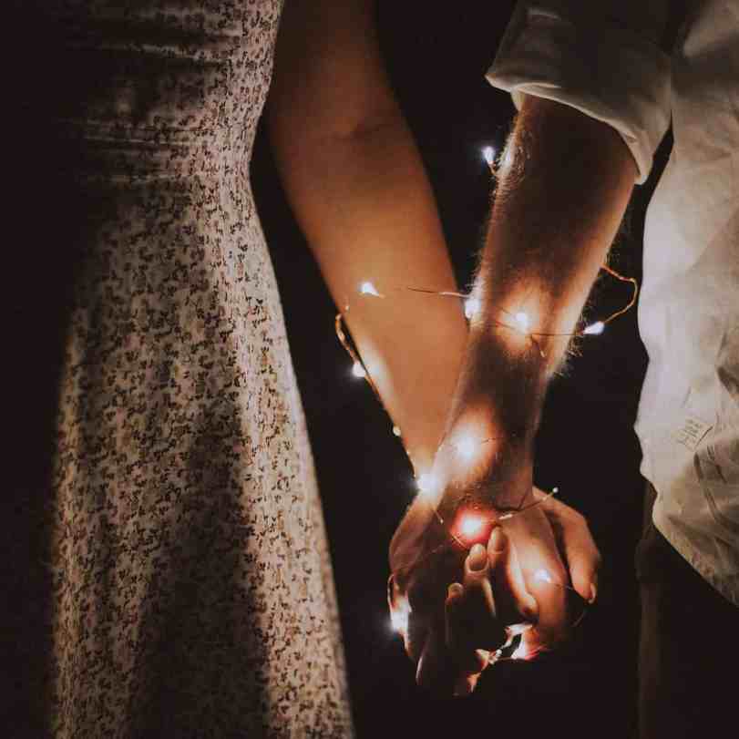 Casal de mãos dadas com luzes pisca pisca enroladas no braço