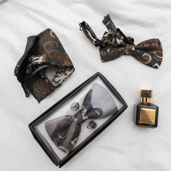 Abotoadura, gravata, perfume  e gravata de um homem em cima de um lençol