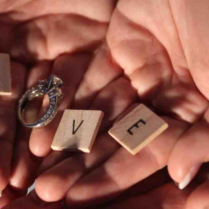 Mulher segurando bloquinhos de madeira escrito a palavra love, sendo o "o" substituído pelo anel de noivado