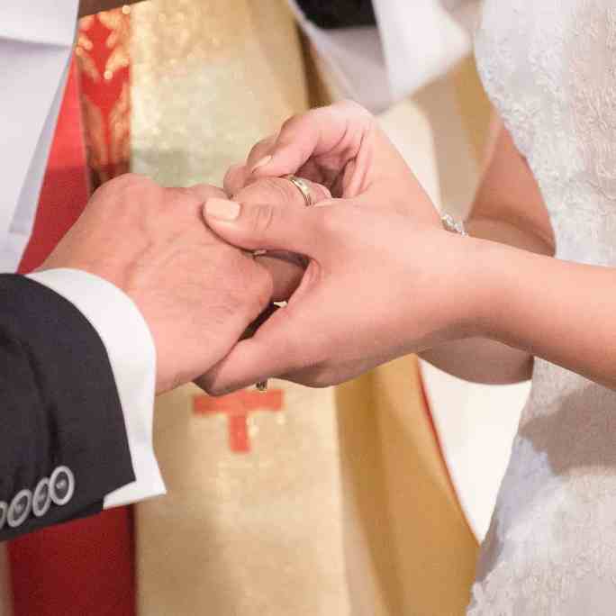 Quem deve pagar as alianças de casamento? - Pagar as aliancas de casamento Noiva colocando aliança de casamento na mão do noivo em frente ao padre