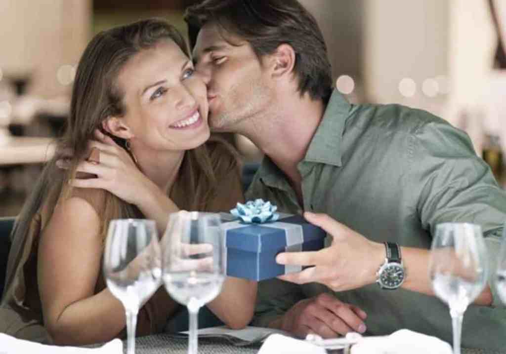 Homem entregando presentes e dando beijo na bochecha de mulher
