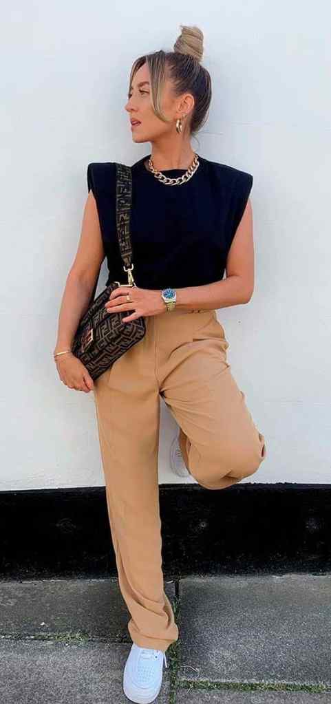 7 Estilos Universais: Quais Joias combinam com Cada um Deles? - Estilo natural esportivo 3 Mulher usando blusa preta, calça bege, bolsa, coque e joias