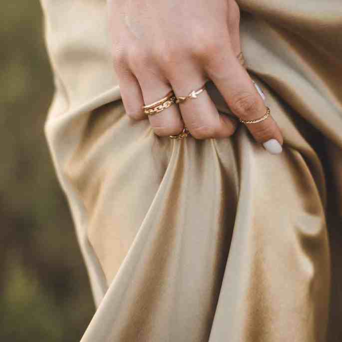 Mulher de vestido de seda bege usando anel na mão esquerda- qual o significado do anel em cada dedo?