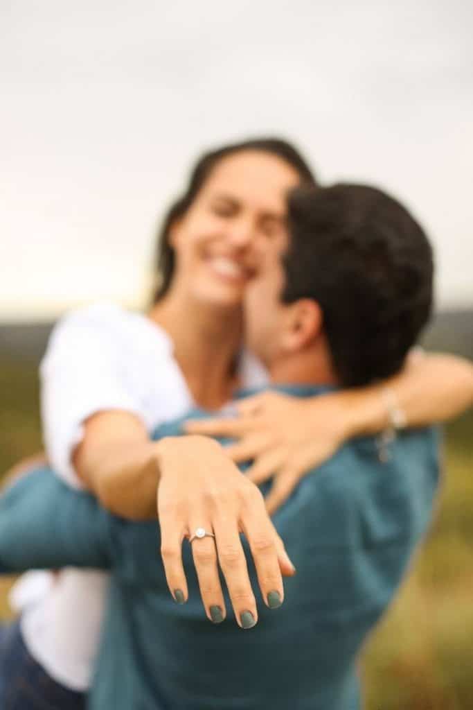 Casal abraçados, ela está mostrando o anel de noivado na mão