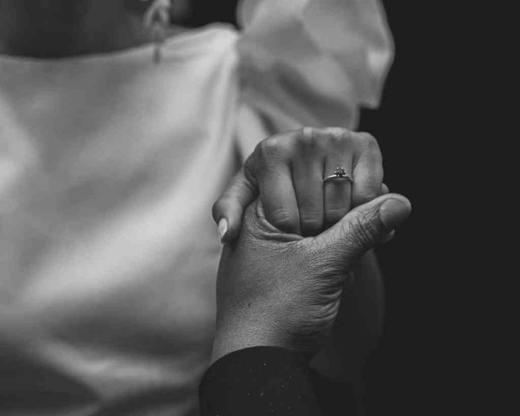 Foto em preto e branco de homem segurando mão da mulher que está usando anel de noivado