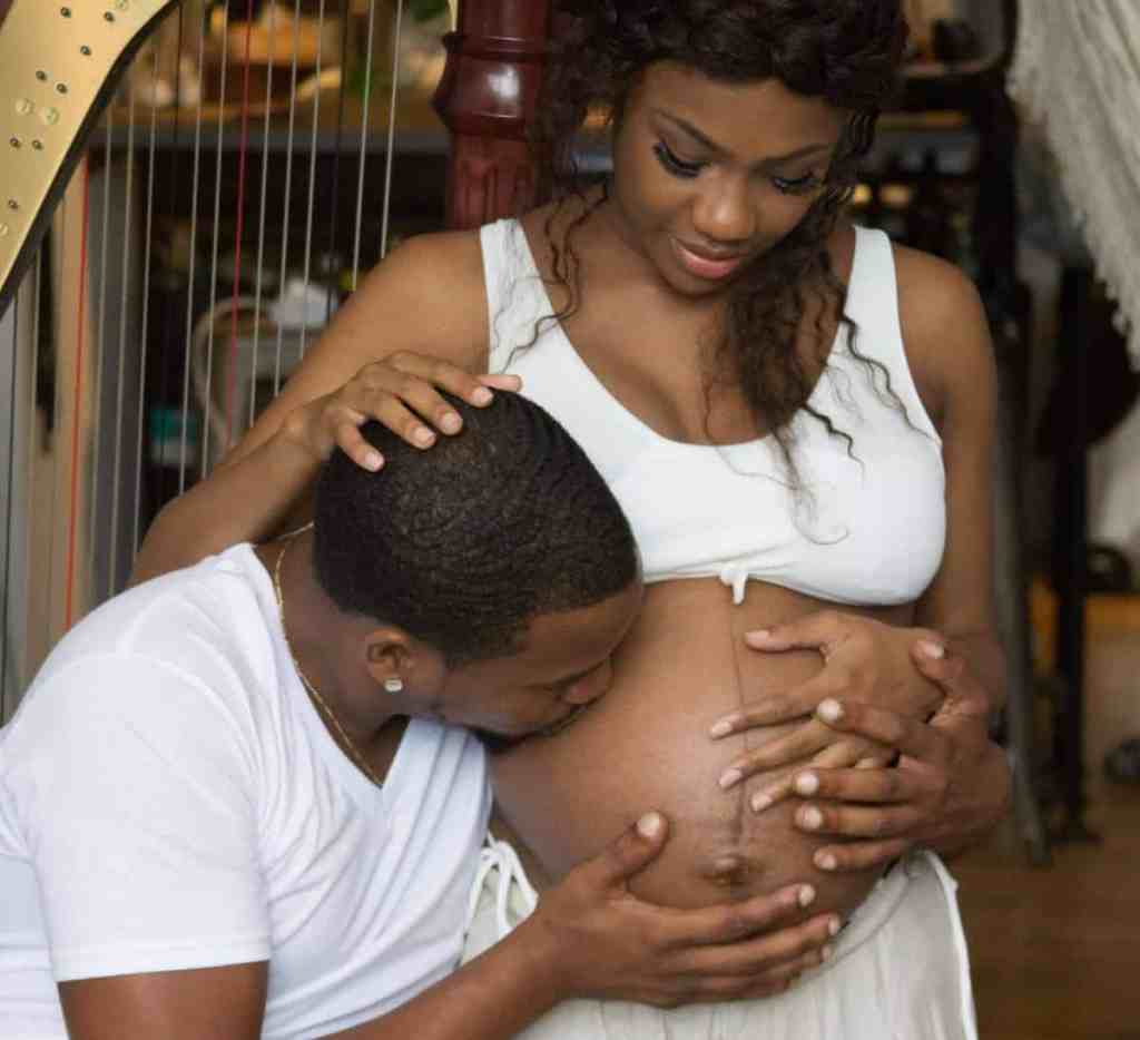 Mulher grávida com a mão na barriga, e o marido beijando a barriga