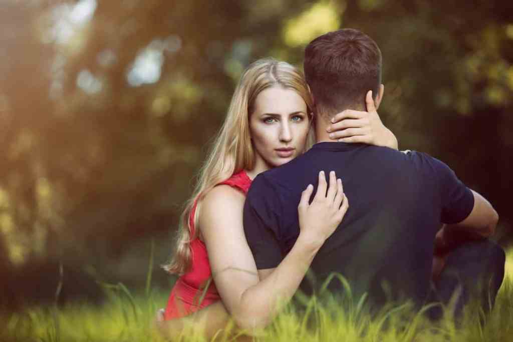 Mulher loira e homem de camiseta azul sentados no chão de grama abraçados - dar um tempo no relacionamento funciona?