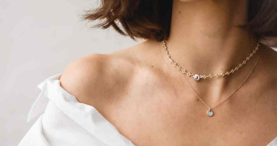 Mulher usando dois colares de ouro e blusa branca aberta