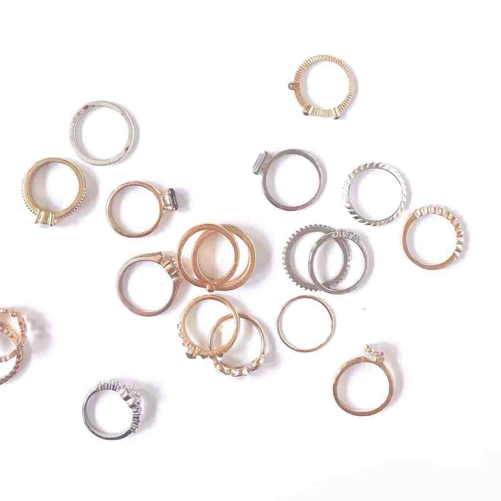 Imagem com fundo branco em que estão espalhados vários anéis na cor dourada e prata