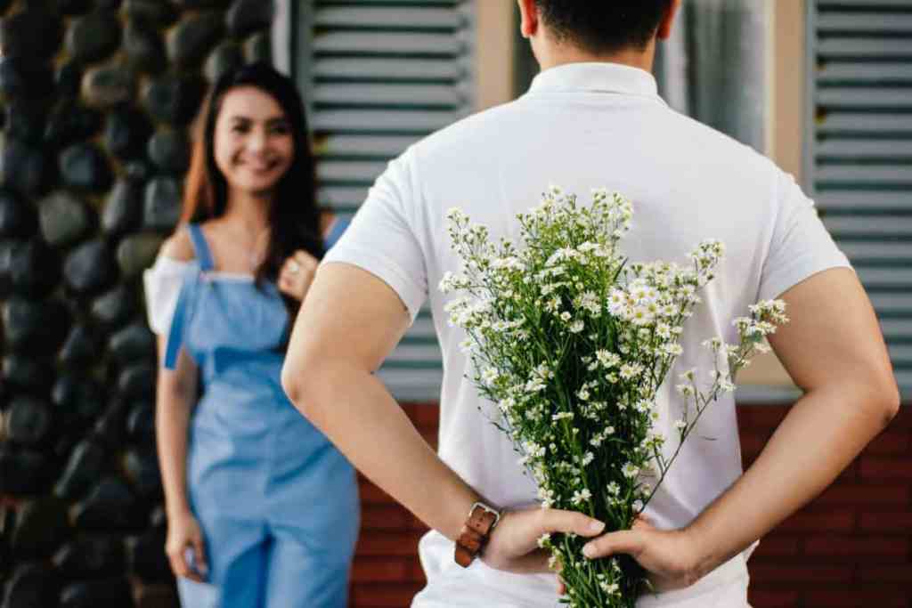 Homem segurando flores atrás das costas para surpreender mulher