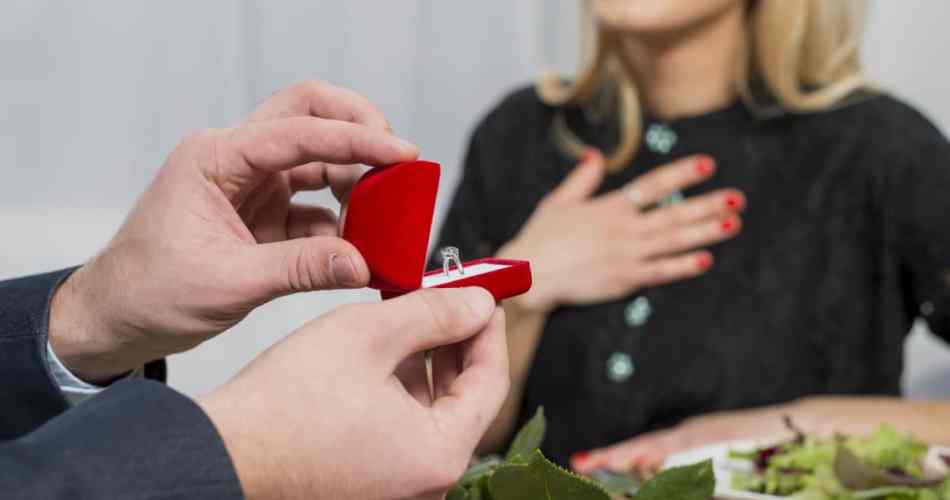 Homem abrindo caixinha vermelha com anel de noivado e pedindo em casamento na mesa de jantar