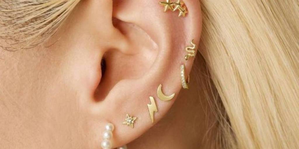 Mulher com vários piercings dourados na orelha.