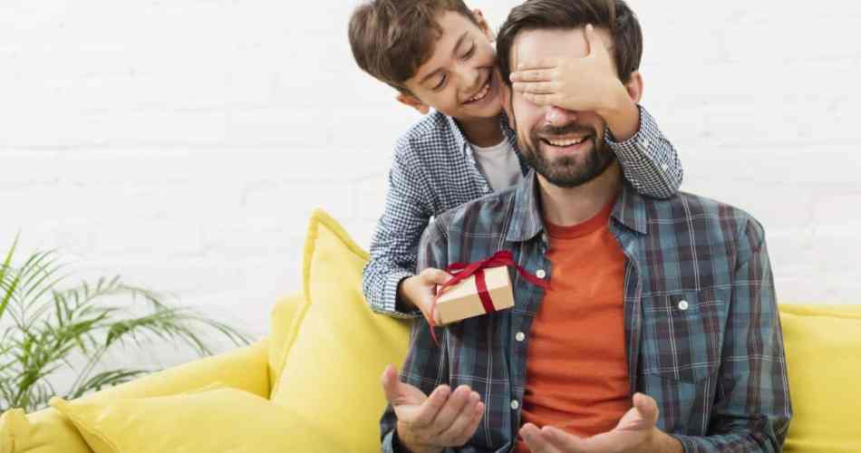 Filho entregando presente para o pai enquanto tampa os olhos dele pra fazer surpresa