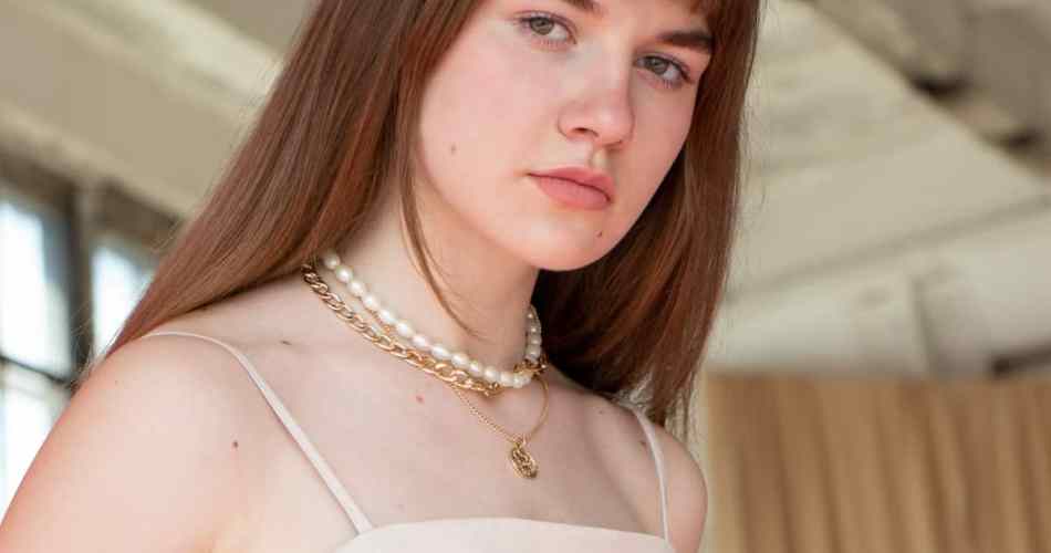 Mulher de cabelo longo liso e franja usando blusa regata e colares de pérolas