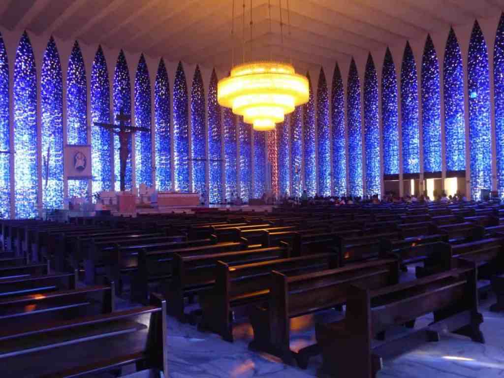 Santuário dom bosco possui vitrais azuis e uma grande cruz no centro, na foto a igreja está vazia
