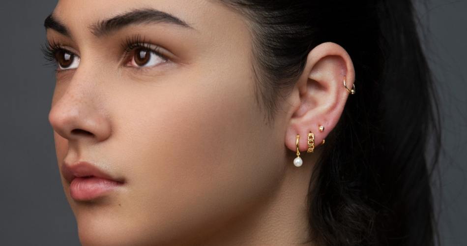 Garota branca com cabelo em rabo de cavalo usando brincos pequenos e piercings