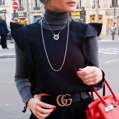 Mulher na rua usando colares prata e blusa de gola alta preta
