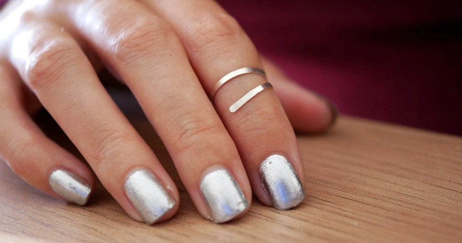 Mão feminina com unhas pintadas de prata e usando anéis de falange prata