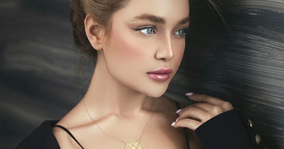 Mulher loira de coque, usando regata e cardigã preto, ela usa um colar de ouro com pingente