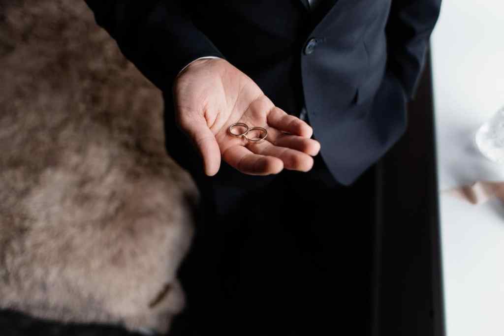 Homem segurando na palma da mão duas alianças - alianças precisam combinar? Venha entender melhor!