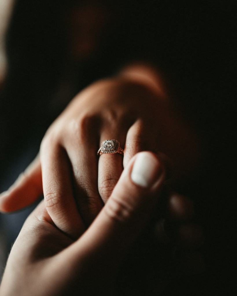 Homem segurando mão da noiva com anel de noivado - qual anel de noivado com pedra colorida escolher?