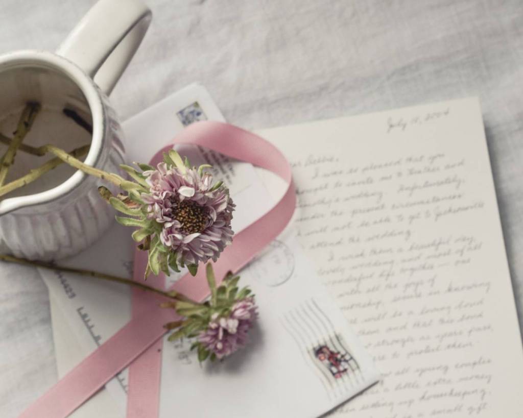 Em cima da mesa há uma carta de amor e um envelope com laço rosa, flores e caneca por cima - 16 ideias de joias para namorado ou namorada