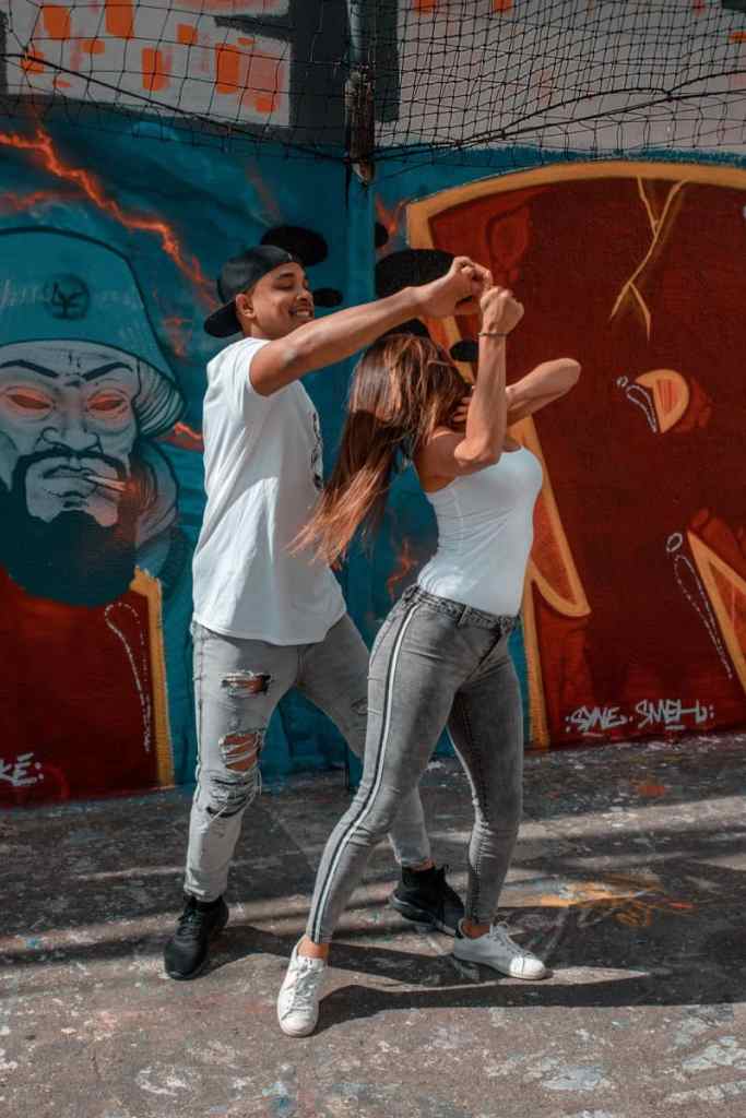 Homem e mulher estão dançando juntos em frente a parede com grafitti na rua