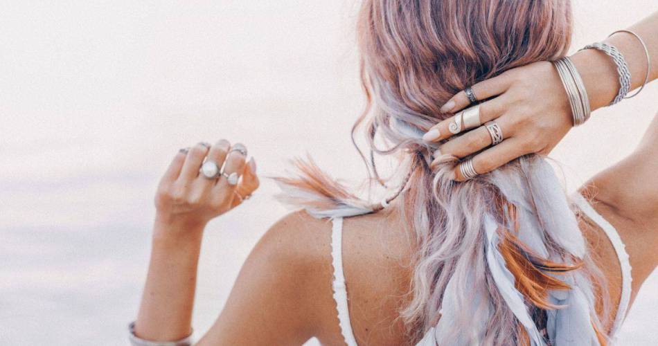 Mulher na praia de costas segurando o cabelo, de modo que está visível seus anéis e pulseiras