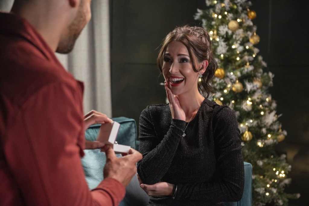 Mulher sendo pedida em casamento em frente árvore de natal