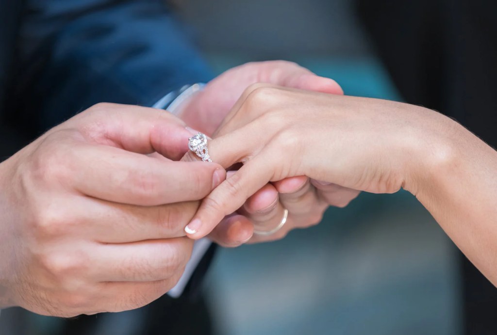 Homem colocando anel de noivado em ouro branco na mão da noiva